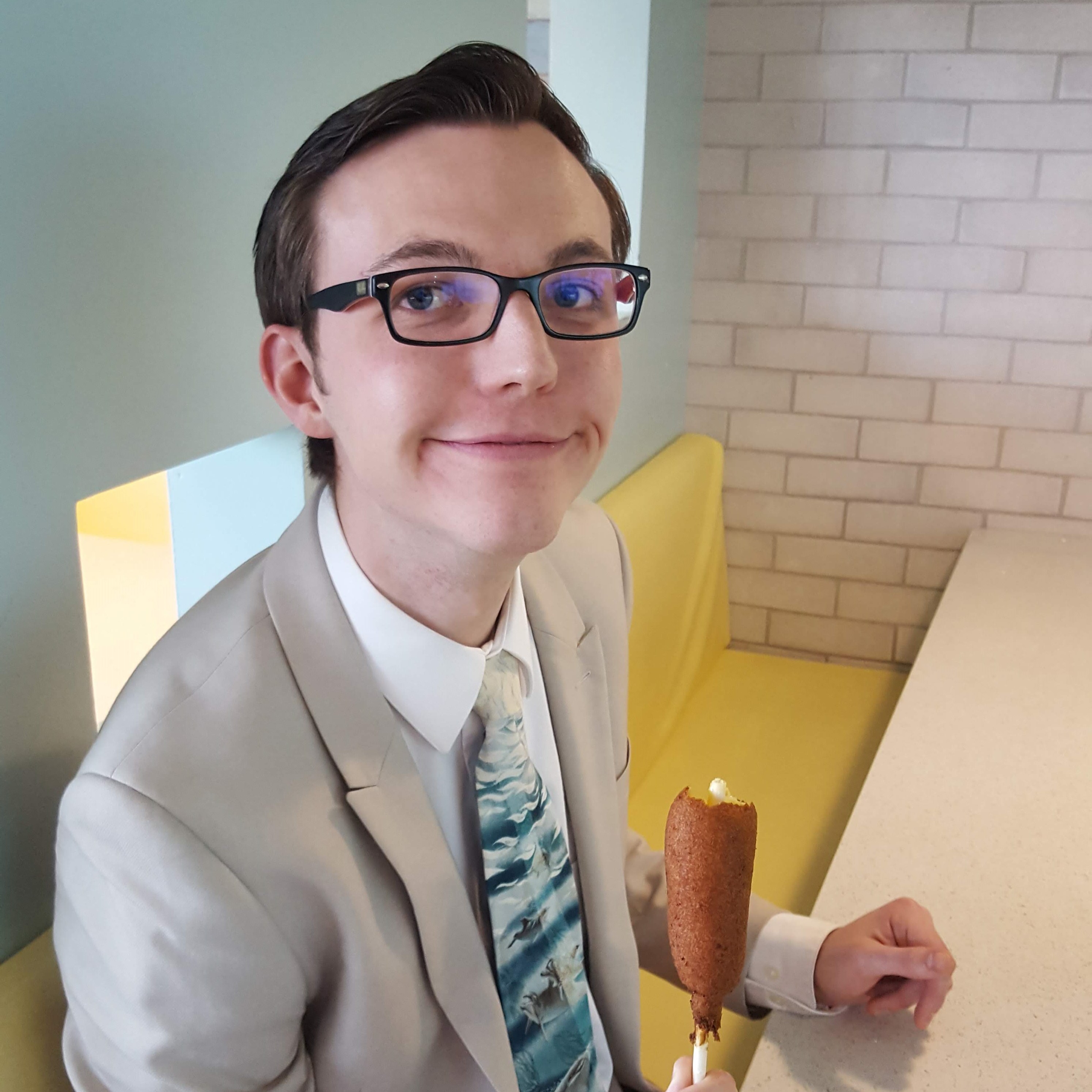 Photo of me in a tan suit eating a corn dog